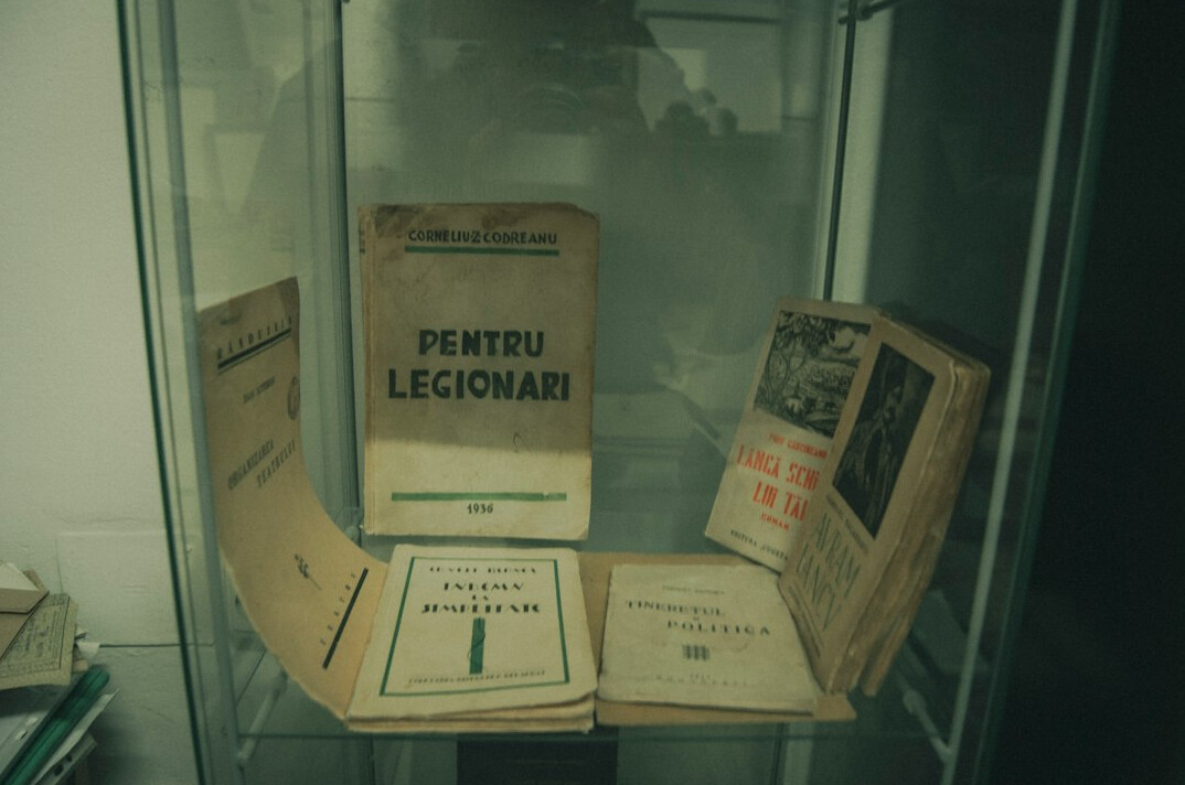 Old case file documents and photographs spread on a wooden table with a magnifying glass